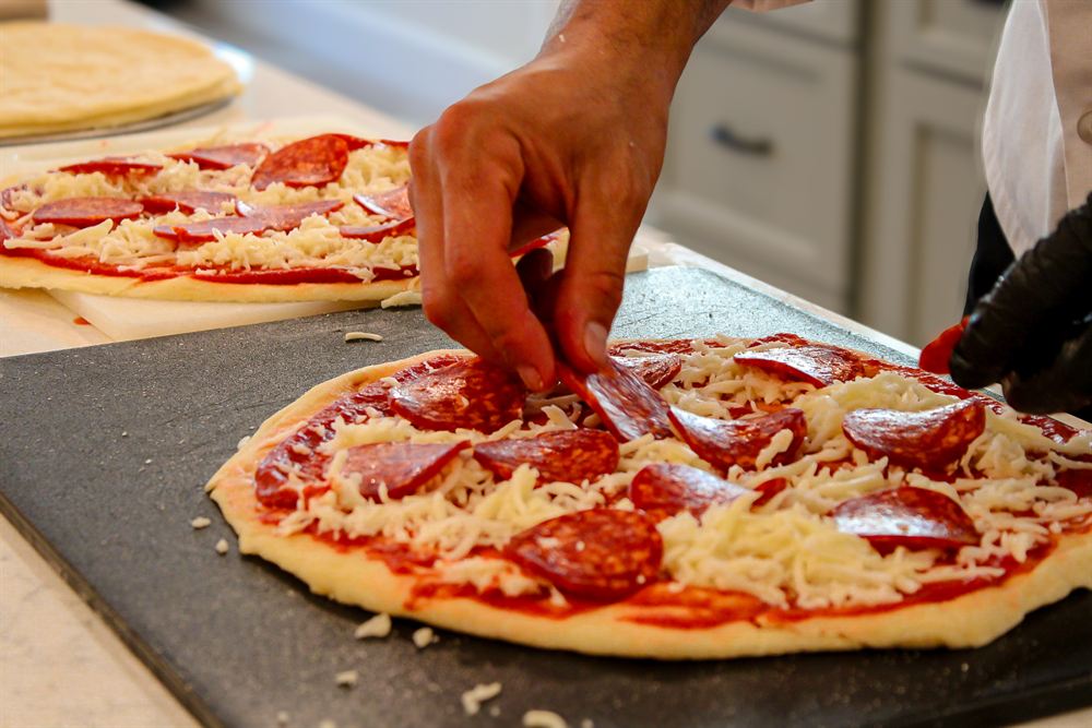 Chef Kaynan hand-topping a fresh pizza for a pizza party
